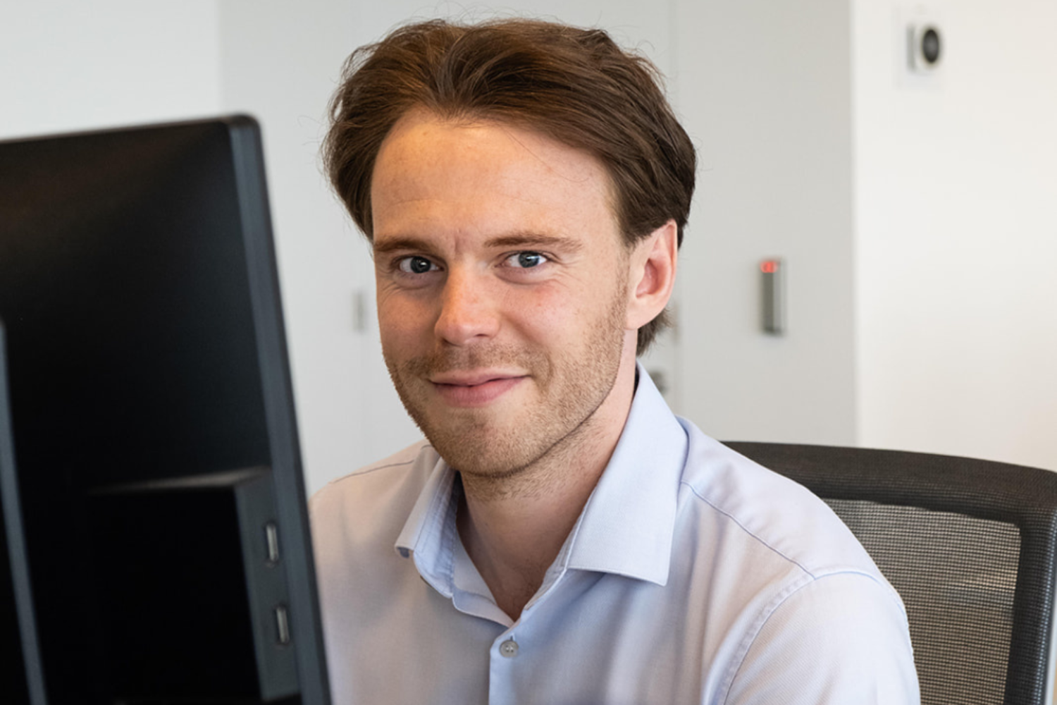 Man sitting at his desk, looking at the camera and smiling.