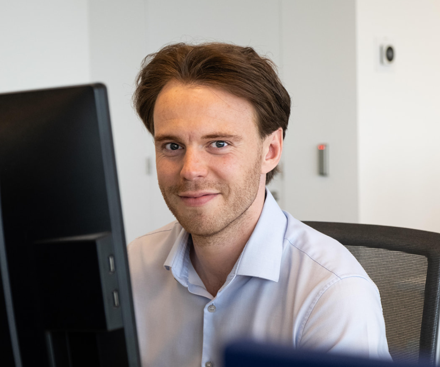 Man sitting at his desk, looking at the camera and smiling.