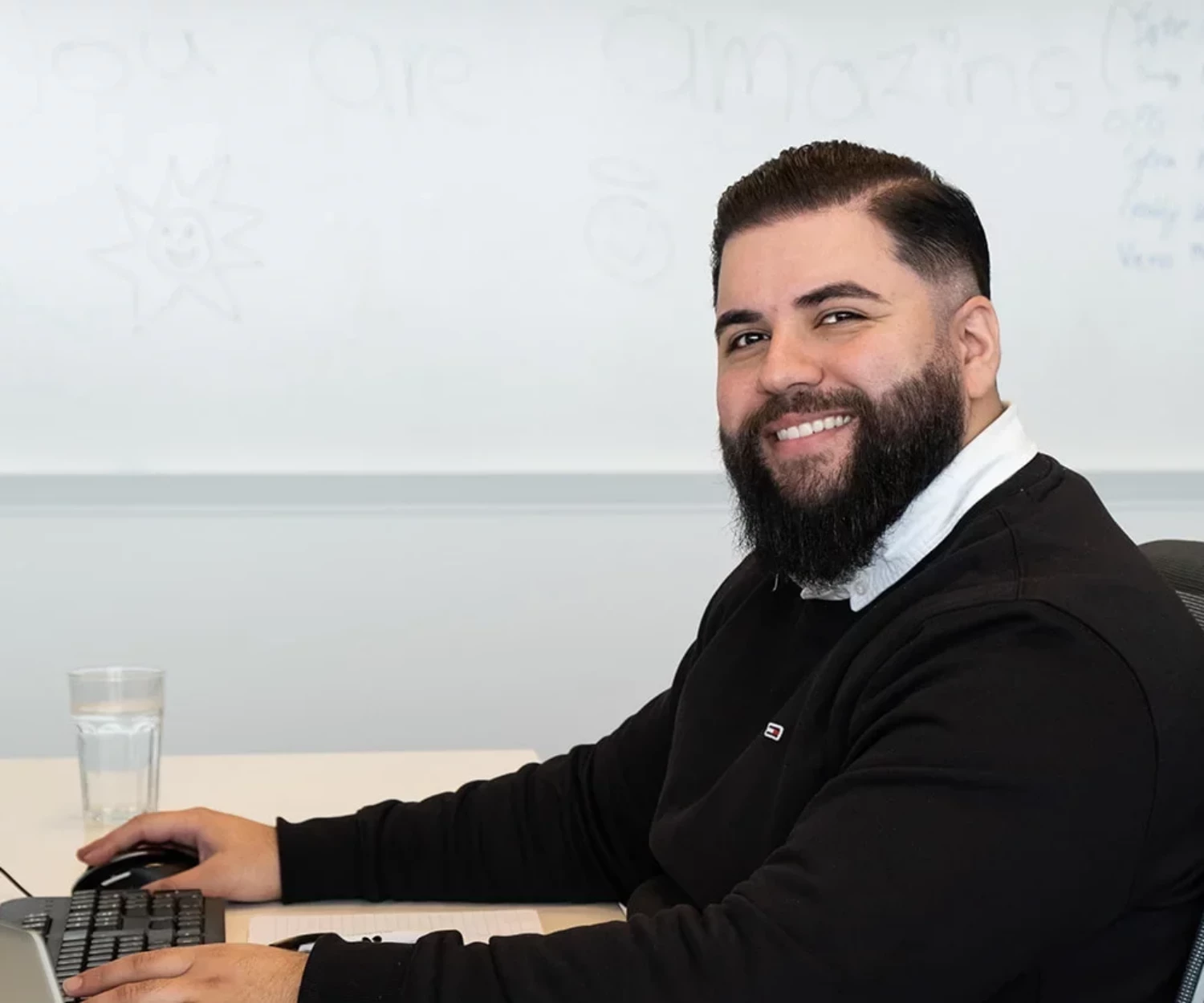 Man sitting at his desk, looking at the camera and smiling.