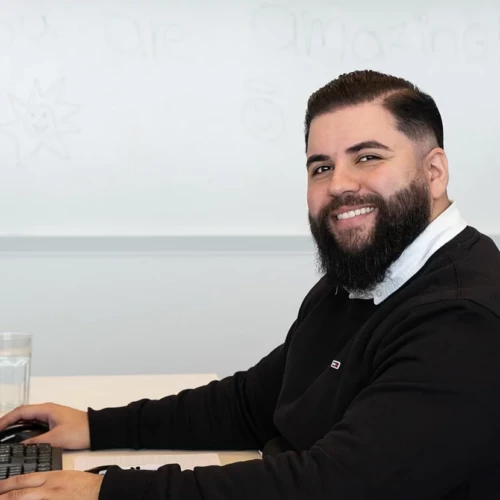 Man sitting at his desk, looking at the camera and smiling.