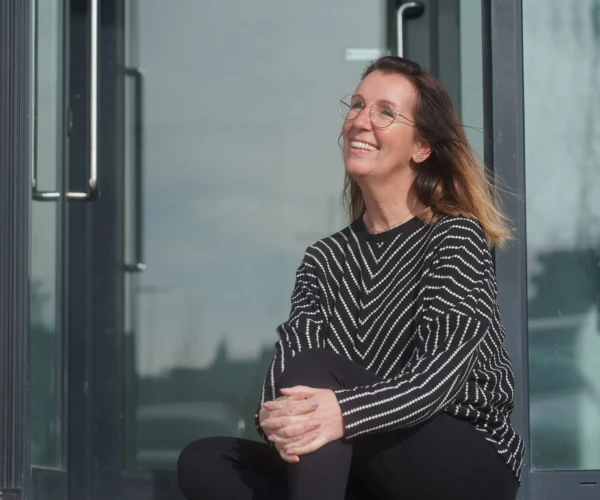 Woman smiling outside a building in the sunlight.